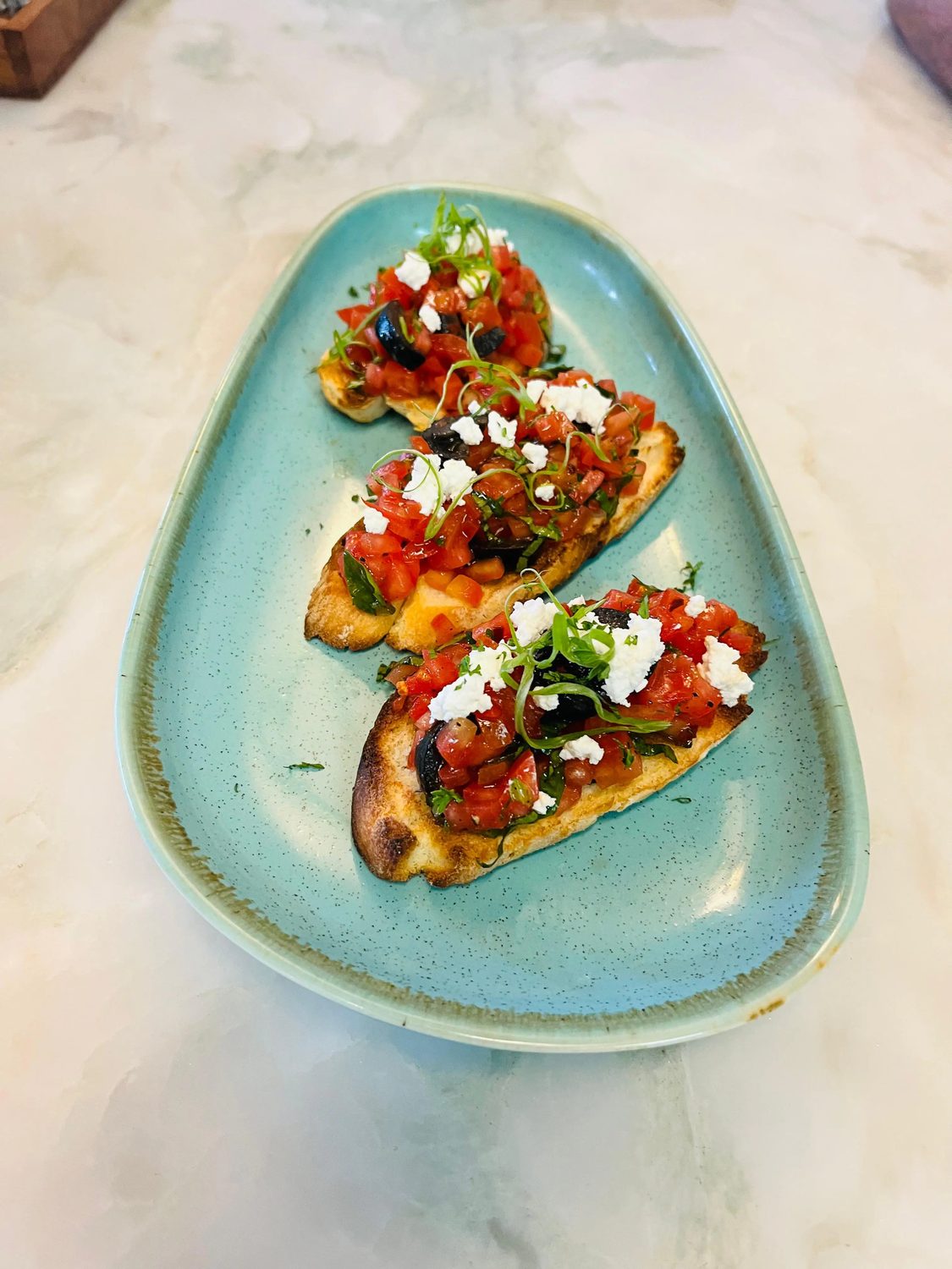 Bruschetta al pomodoro with feta on a green ceramic platter